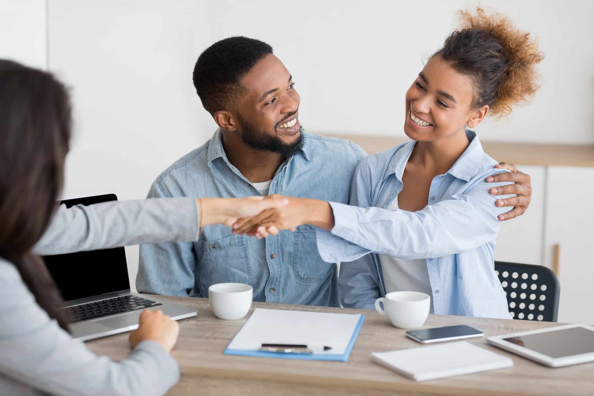 cheerful afro spouses and finansial counselor handshaking in office